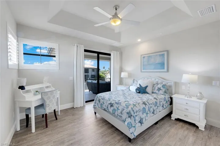 Bedroom featuring a raised ceiling, light wood-style floors, access to exterior, and ceiling fan