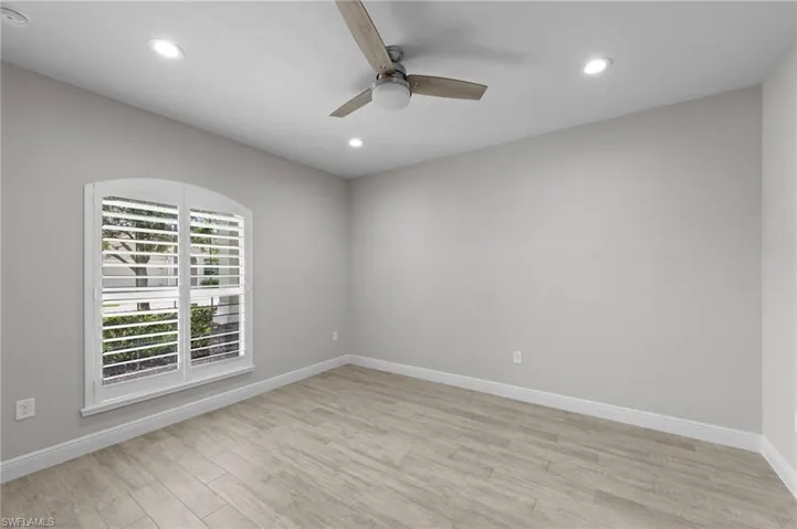 Room featuring a window with arched transom and white plantation shutters, wood-finish flooring, recessed lighting, a ceiling fan with light, and light gray wall paint