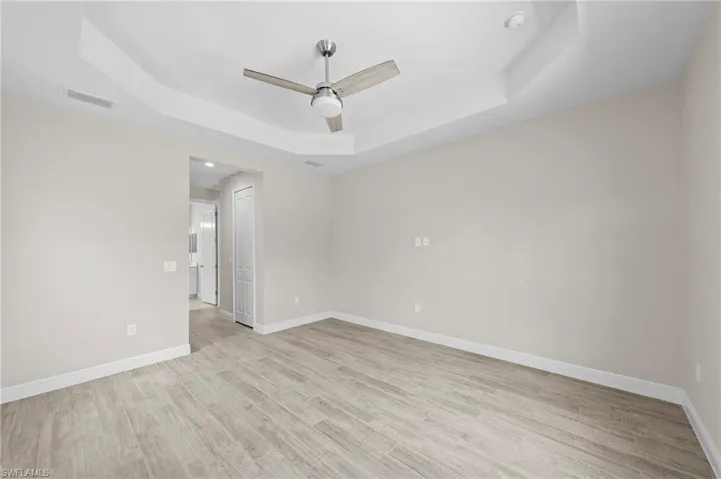 Spacious room featuring light wood-finish flooring, a contemporary ceiling fan, and a tray ceiling