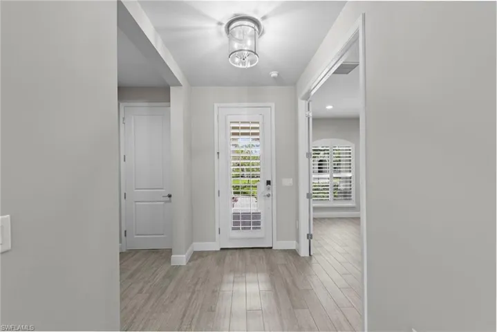 Entryway featuring wood-finish flooring, a contemporary semi-flush mount light fixture, white interior doors, and a glass-paneled exterior door with plantation shutters