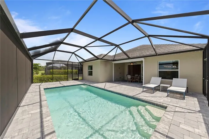 Screened-in pool area featuring a rectangular swimming pool with integrated steps, surrounded by paver decking