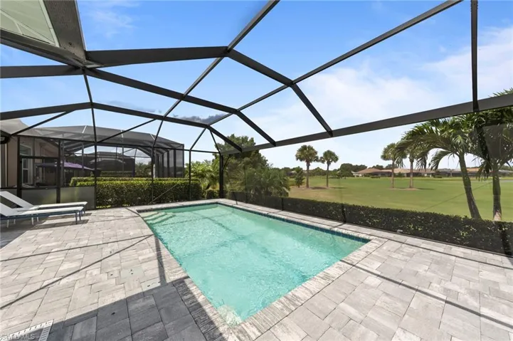 Screen-enclosed rectangular pool area featuring paver decking, integrated pool steps, and a privacy hedge bordering a manicured green space