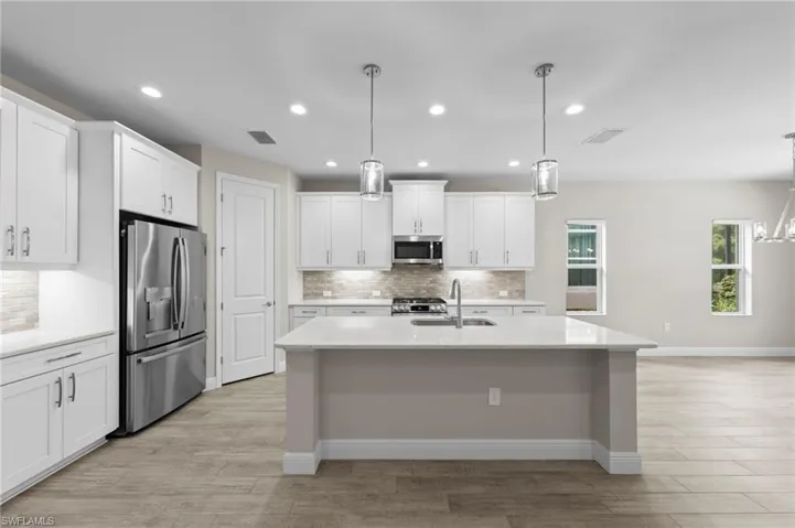 Modern kitchen featuring a central island with a sink, white cabinetry, stainless steel appliances, and wood-finish flooring
