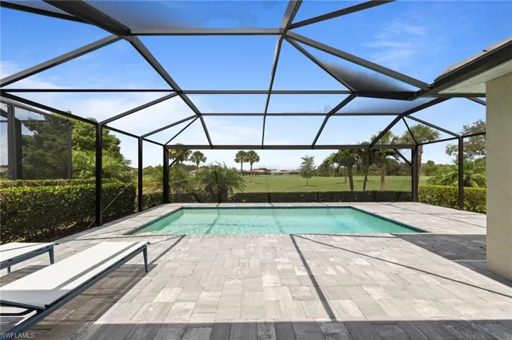 Screened lanai featuring a swimming pool, extensive paver decking, and a low hedge border