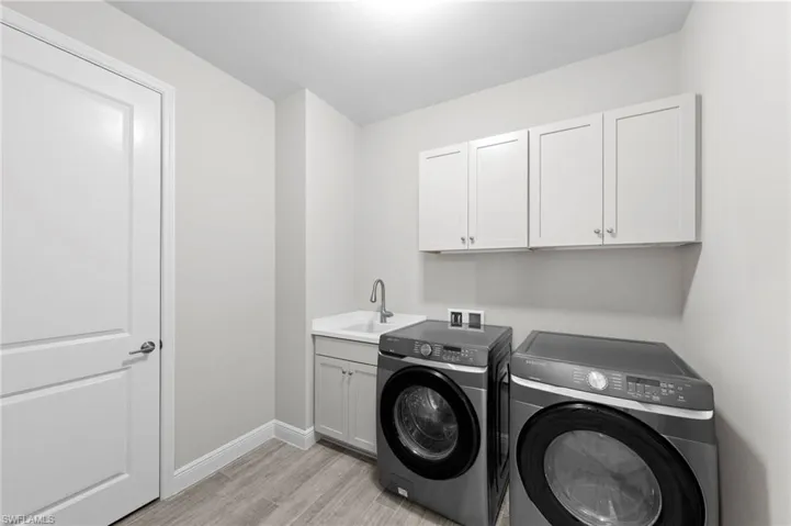 Dedicated laundry room featuring light wood-finish flooring, white wall cabinetry, a utility sink with a gooseneck faucet, and white baseboard trim