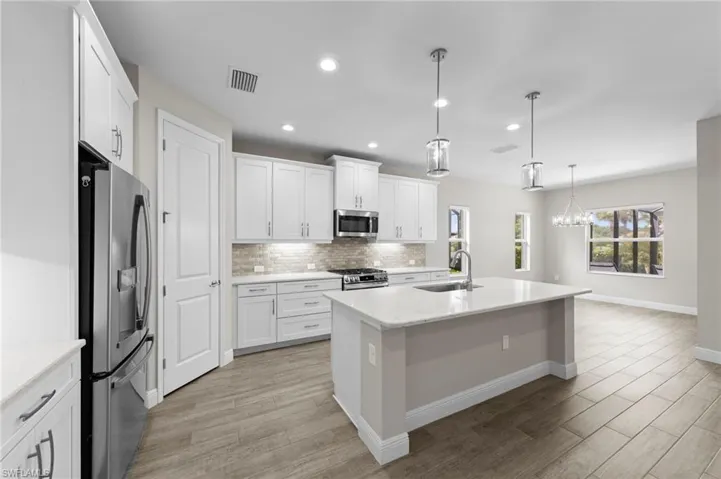 Contemporary kitchen featuring white shaker cabinetry, stainless steel appliances, a center island with sink, quartz countertops, and wood-finish flooring