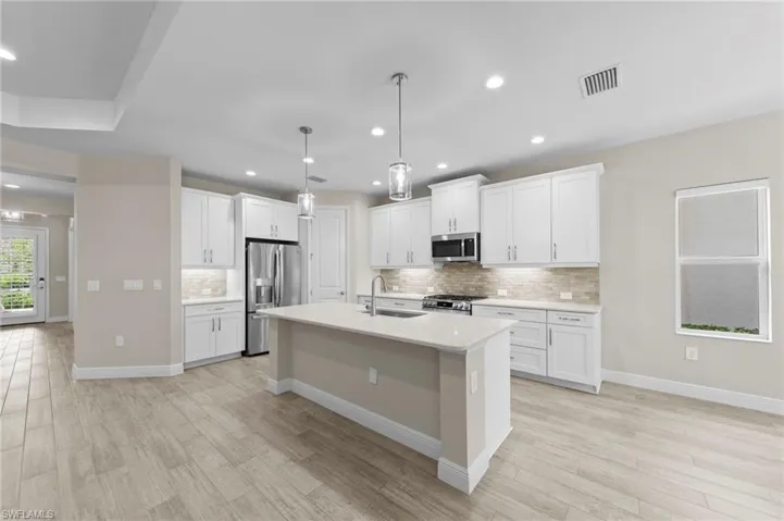 Contemporary kitchen featuring an expansive island with a light-toned countertop, white cabinetry, stainless steel appliances, and wood-finish flooring