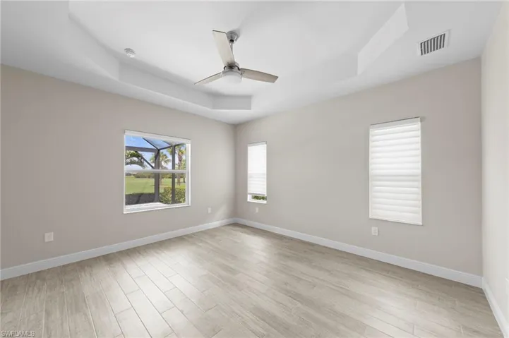 Spacious room featuring light wood-finish flooring, neutral wall tones, and a tray ceiling with a modern ceiling fan