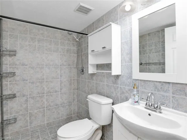 Bathroom featuring tasteful backsplash, vanity, a textured ceiling, tile walls, and toilet