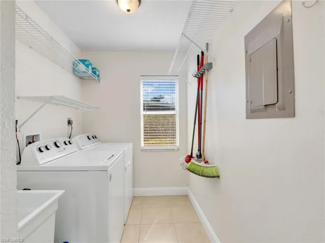 Laundry room featuring light tile patterned floors, electric panel, washer and clothes dryer, and sink