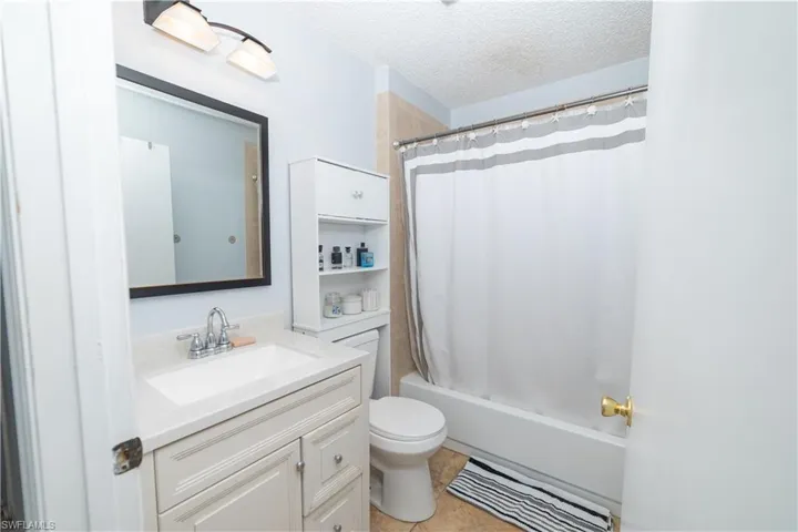 Full bathroom with tile patterned floors, vanity, a textured ceiling, shower / bathtub combination with curtain, and toilet