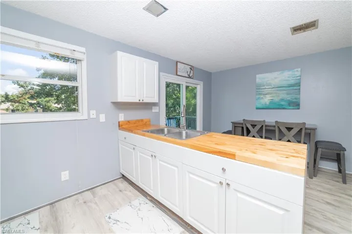Kitchen with wood counters, white cabinets, sink, light hardwood / wood-style flooring, and a textured ceiling