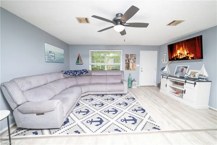 Living room with ceiling fan, light wood-type flooring, and a textured ceiling