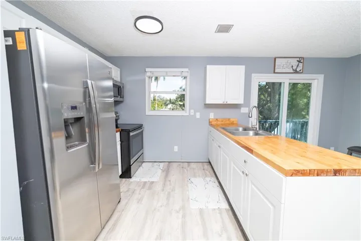 Kitchen with white cabinets, appliances with stainless steel finishes, a textured ceiling, and butcher block countertops