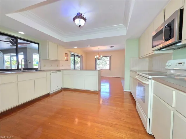 Kitchen with backsplash, white appliances, a tray ceiling, ornamental molding, and light wood-style floors