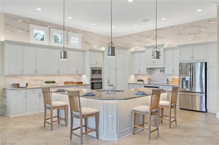 Kitchen featuring a large island with sink, decorative light fixtures, ornamental molding, and stainless steel appliances