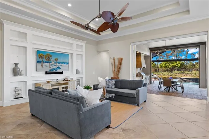 Living room with light tile floors, ornamental molding, ceiling fan, and a raised ceiling
