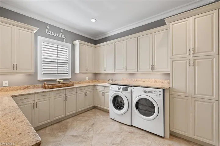 Clothes washing area with ornamental molding, washing machine and clothes dryer, cabinets, and light tile floors