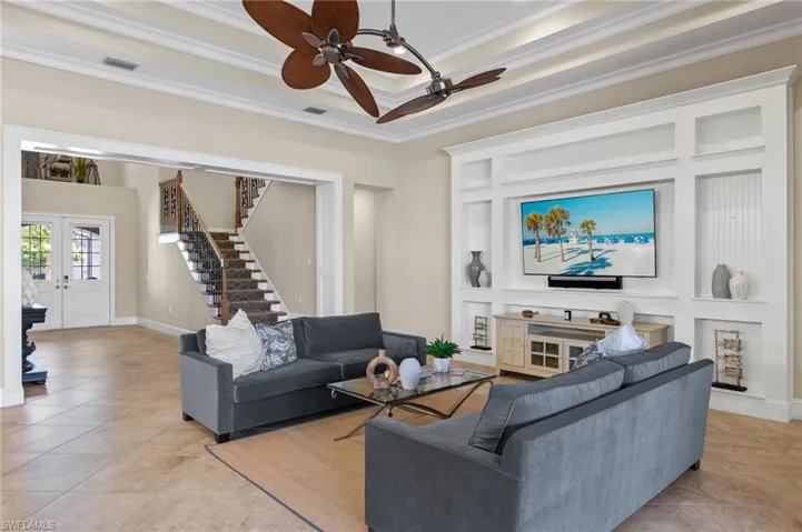 Tiled living room featuring a tray ceiling, crown molding, french doors, and ceiling fan