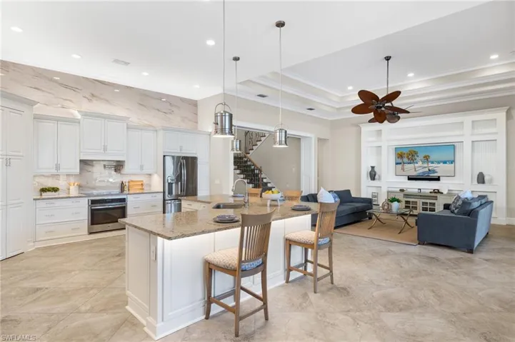 Kitchen featuring appliances with stainless steel finishes, a tray ceiling, white cabinets, a large island with sink, and ceiling fan