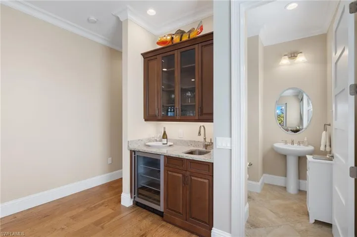 Bar featuring light hardwood / wood-style floors, crown molding, light stone counters, wine cooler, and sink