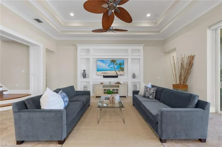 Tiled living room featuring ceiling fan, a raised ceiling, and crown molding
