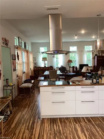 Kitchen featuring white cabinetry, island range hood, black stovetop, dark hardwood / wood-style flooring, and decorative light fixtures
