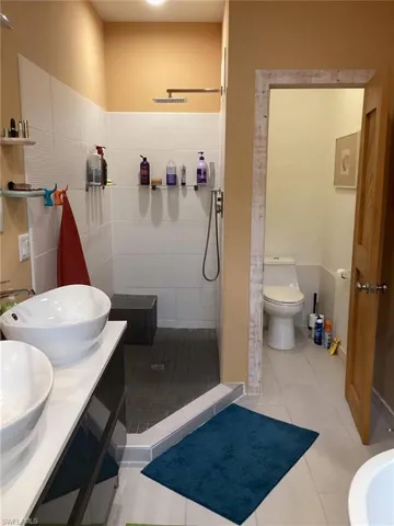 Bathroom with tiled shower, vanity, toilet, and tile patterned flooring