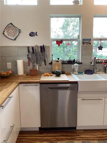Kitchen featuring sink, dishwasher, white cabinets, wood counters, and decorative backsplash