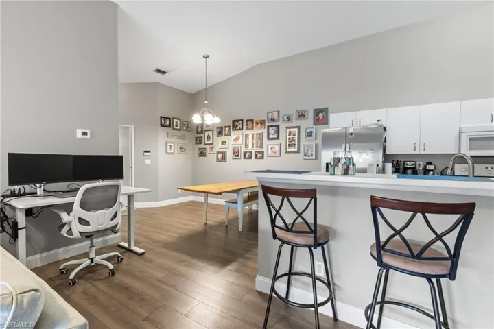 Kitchen with dark wood-type flooring, a breakfast bar area, white cabinetry, hanging light fixtures, and stainless steel refrigerator