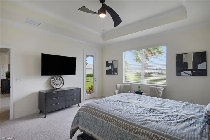 Bedroom featuring a raised ceiling, crown molding, light carpet, access to exterior, and a ceiling fan