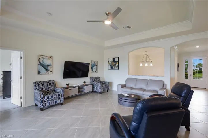 Living area with light tile patterned floors, crown molding, a raised ceiling, ceiling fan, and arched walkways
