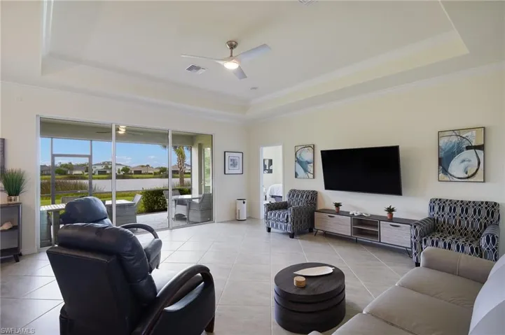 Living area featuring a raised ceiling, a ceiling fan, light tile patterned flooring, and ornamental molding