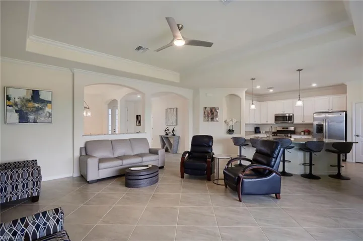 Living room with ornamental molding, light tile patterned floors, arched walkways, a tray ceiling, and a ceiling fan