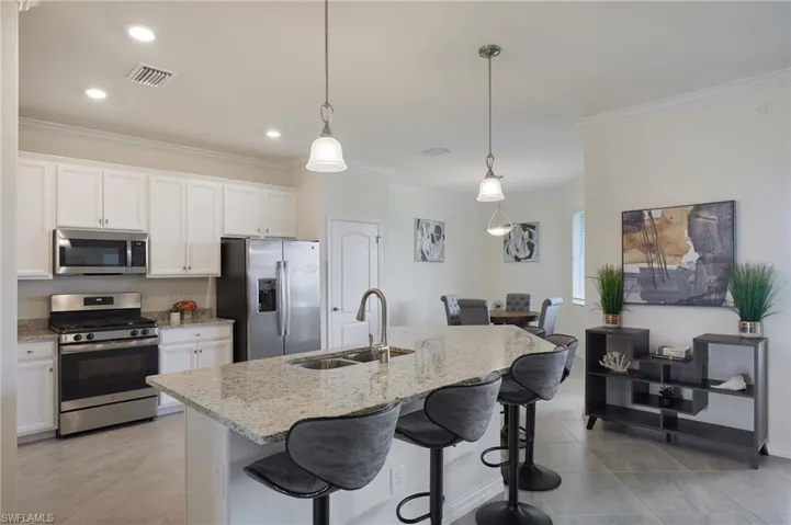 Kitchen featuring appliances with stainless steel finishes, ornamental molding, light stone counters, a kitchen bar, and white cabinetry