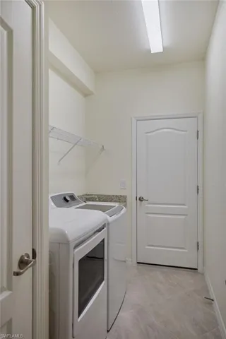 Laundry room with independent washer and dryer and light tile patterned flooring