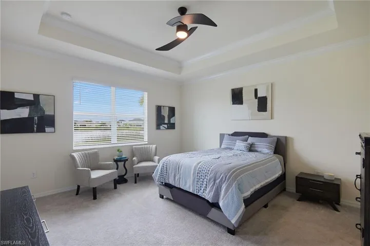 Bedroom featuring a tray ceiling, crown molding, light carpet, and a ceiling fan