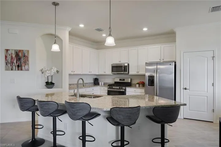 Kitchen featuring stainless steel appliances, crown molding, white cabinets, light stone countertops, and a breakfast bar area