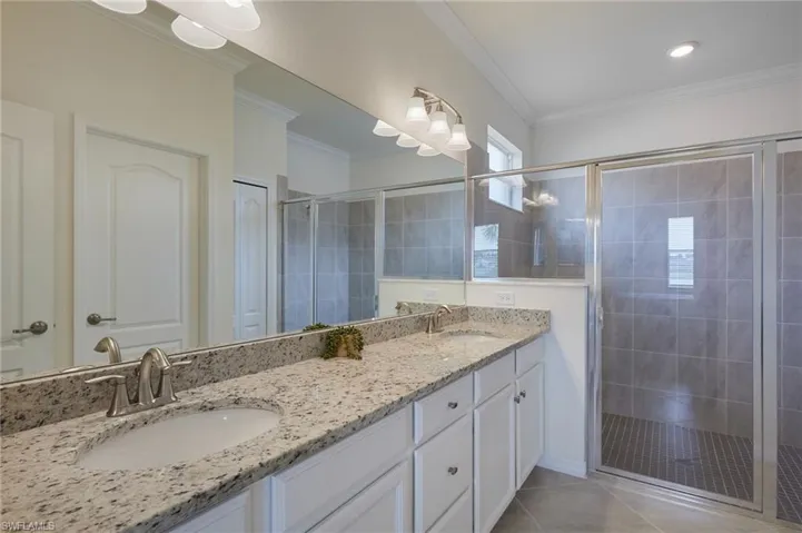 Bathroom featuring a shower stall, double vanity, crown molding, and tile patterned flooring
