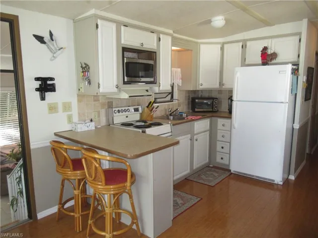 Kitchen featuring white appliances, a kitchen breakfast bar, white cabinetry, a peninsula, and light wood-style flooring