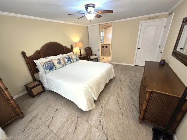 Bedroom with light marble finish flooring, ornamental molding, ceiling fan, and connected bathroom