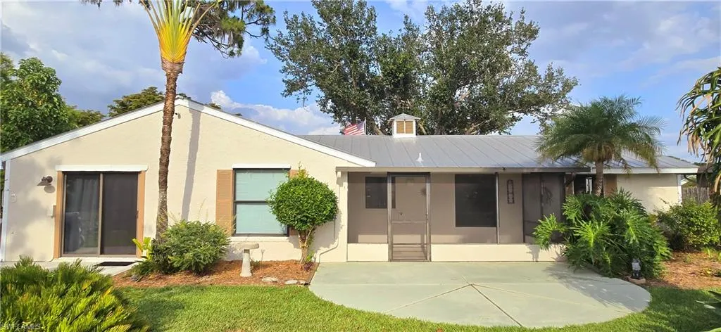 Rear view of house featuring stucco siding, a patio, a chimney, a metal roof, and a lawn