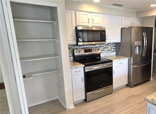 Kitchen with appliances with stainless steel finishes, ornamental molding, white cabinetry, light wood-type flooring, and tasteful backsplash