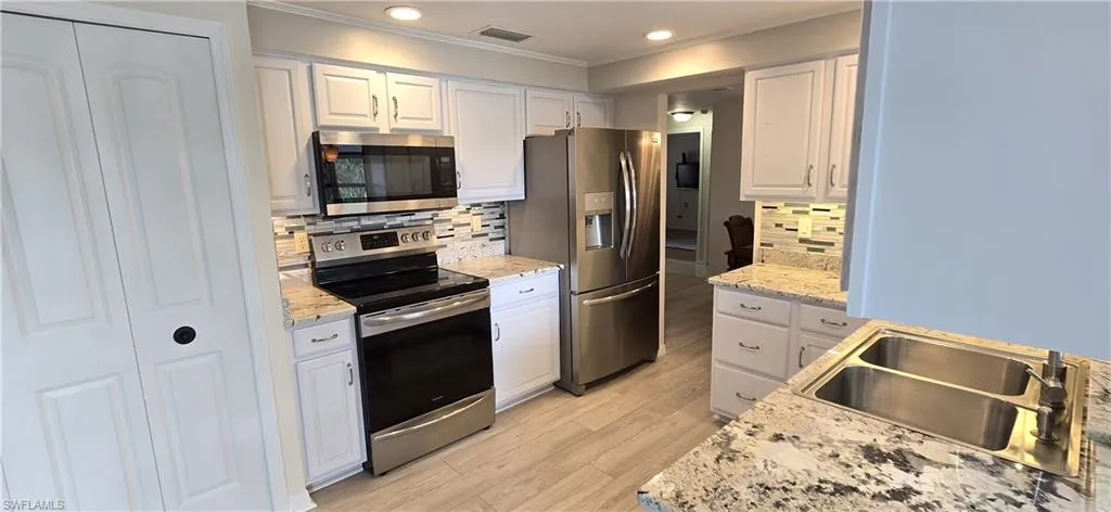 Kitchen with stainless steel appliances, ornamental molding, white cabinetry, light wood-type flooring, and backsplash