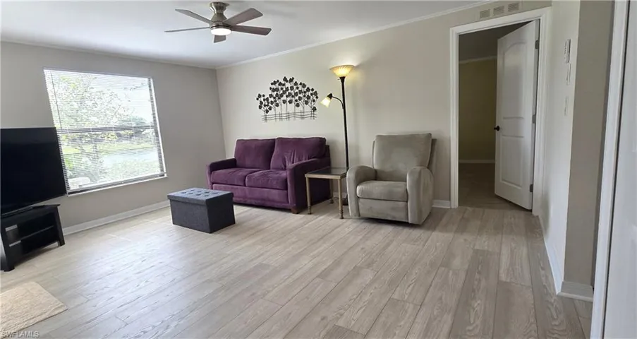 Living room with a ceiling fan, ornamental molding, and light wood-style flooring