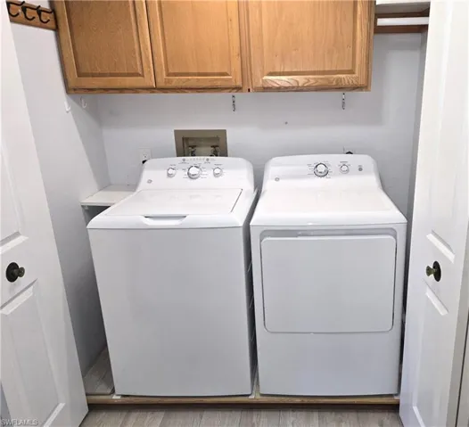 Laundry room with washing machine and clothes dryer, cabinet space, and light wood-type flooring