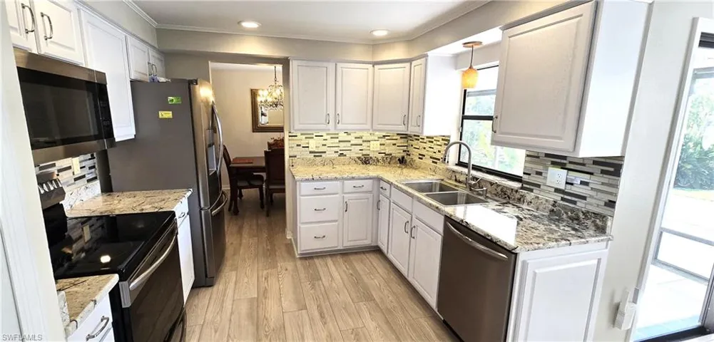 Kitchen featuring appliances with stainless steel finishes, a chandelier, crown molding, light wood-style flooring, and tasteful backsplash
