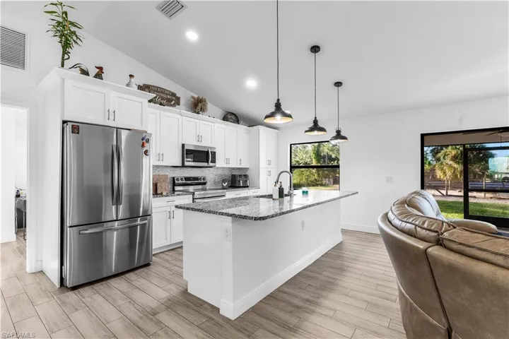 Kitchen featuring white cabinets, pendant lighting, stainless steel appliances, dark stone counters, and a kitchen island with sink