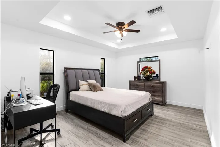 Bedroom featuring multiple windows, light hardwood / wood-style floors, a tray ceiling, and ceiling fan