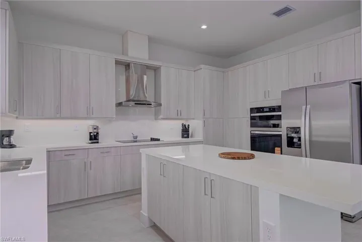 Kitchen with wall chimney range hood, appliances with stainless steel finishes, modern cabinets, light countertops, and a center island